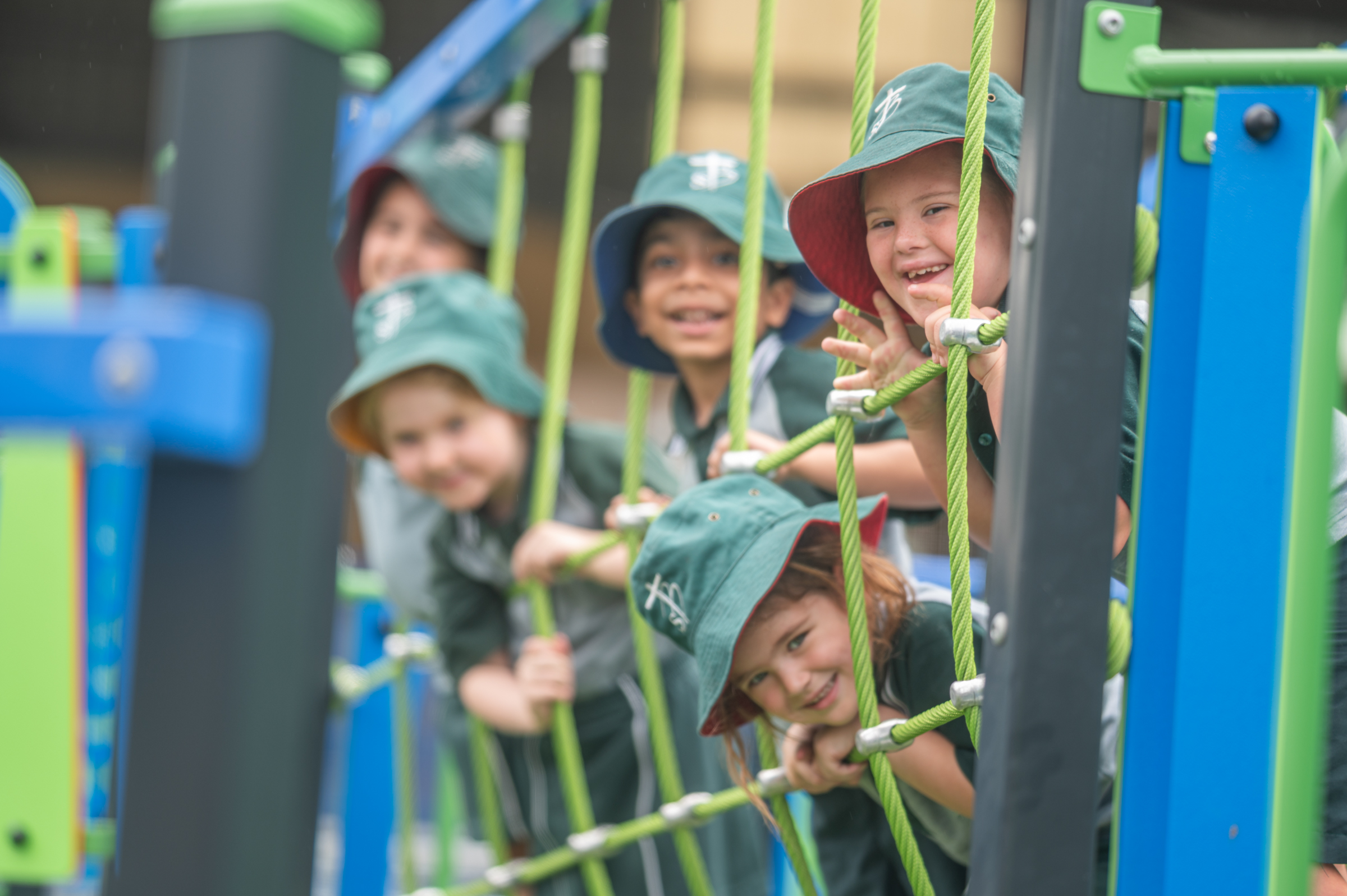 Students in school uniforms climbing rope playground equipment outdoors.